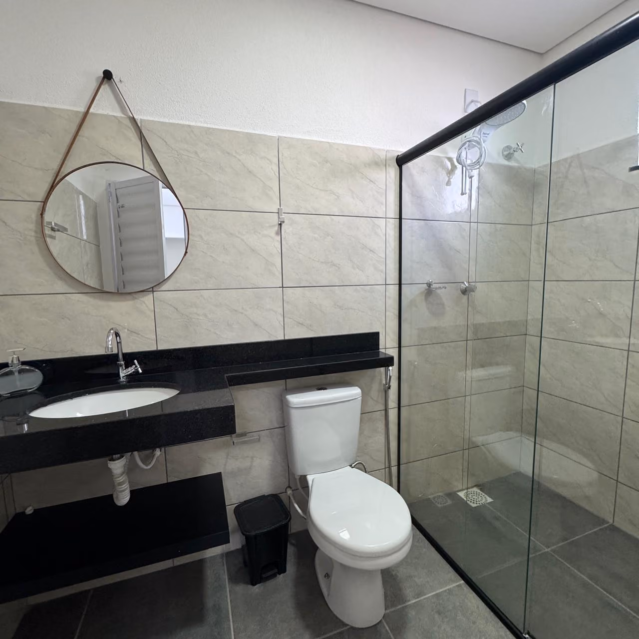 Cozinha compacta com bancada preta, pia de inox, fogão de mesa, armários cinza, geladeira branca, micro-ondas no nicho de prateleira de madeira e decoração com planta verde.